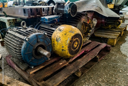 Warehouse of old non-working electric motors on racks and on the floor.