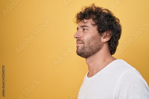 Young hispanic man standing looking to the side over isolated yellow background