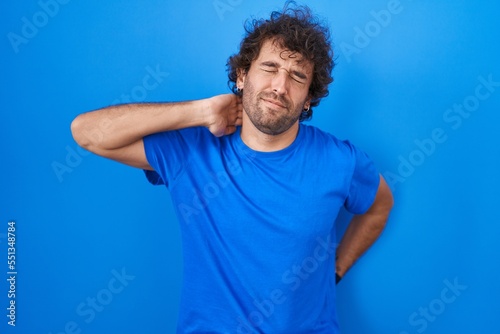 Hispanic young man standing over blue background suffering of neck ache injury, touching neck with hand, muscular pain © Krakenimages.com