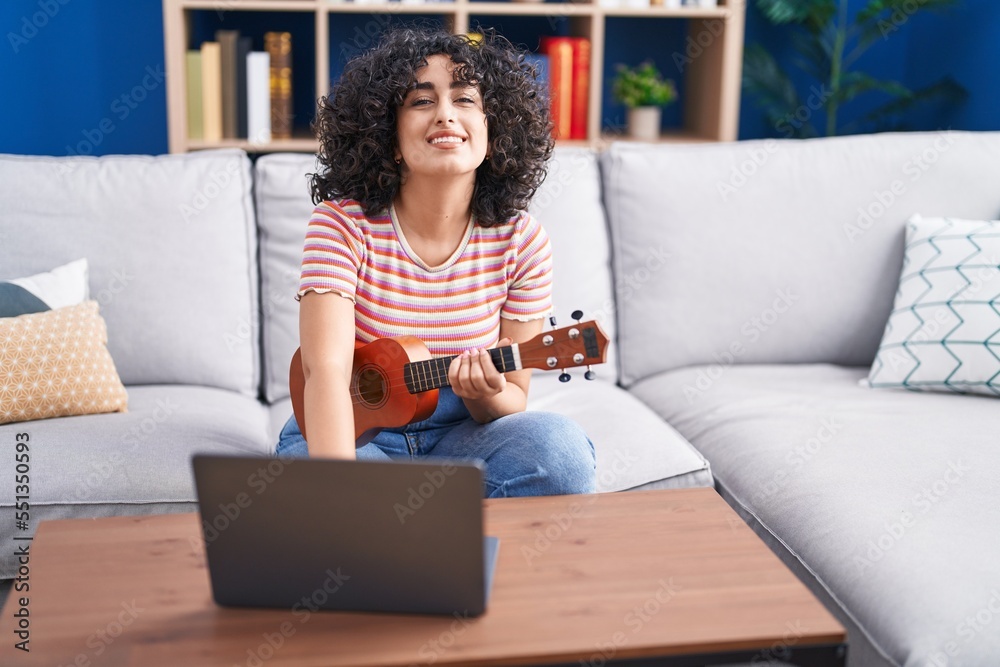 Young middle eastern woman having ukulele online lesson sitting on bed at home Young middle eastern woman having ukulele online lesson sitting on bed at home