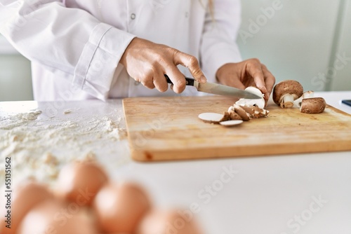Young woman wearing cook uniform cutting mushrooms at kitchen