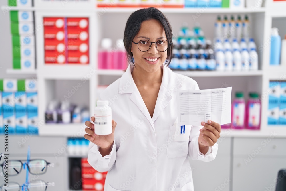 Young hispanic woman pharmacist holding pills bottle and prescription paper at pharmacy Young hispanic woman pharmacist holding pills bottle and prescription paper at pharmacy