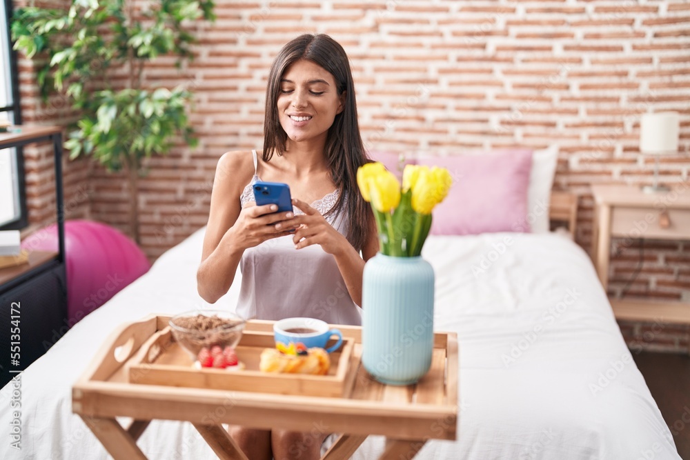 Young beautiful hispanic woman make photo by smartphone to gift breakfast at bedroom