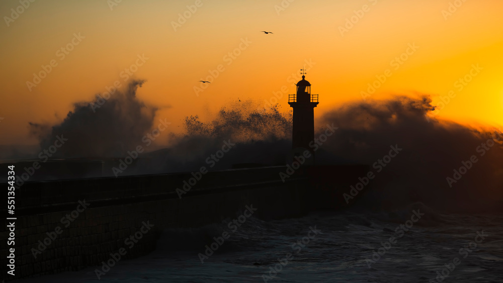View of Lighthouse with huge wave at Atlantic during golden sunset, Porto, Portugal.