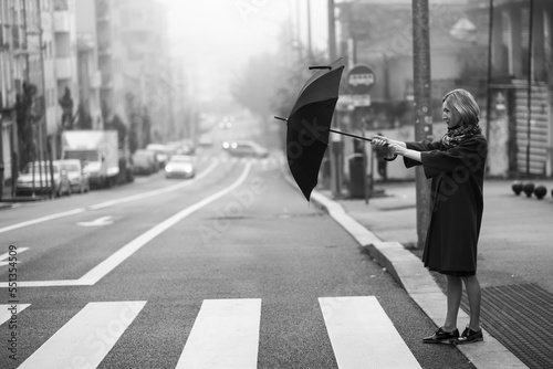 A woman opens an umbrella while crossing the road in the fog. Black and white photo.