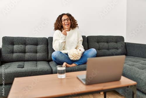 Mature hispanic woman eating popcorn watching tv sitting on the sofa at home