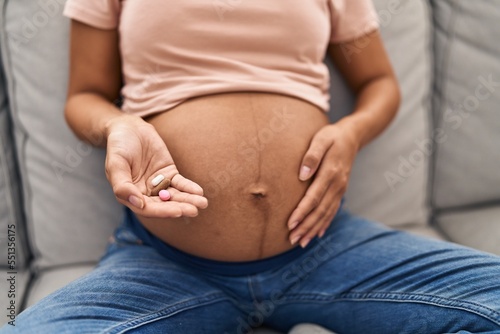 Young latin woman pregnant holding pills at home