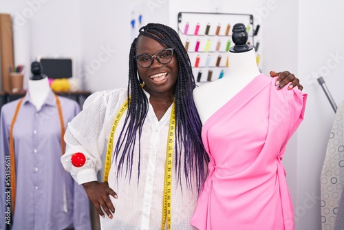 African american woman tailor smiling confident leaning on manikin at tailor shop