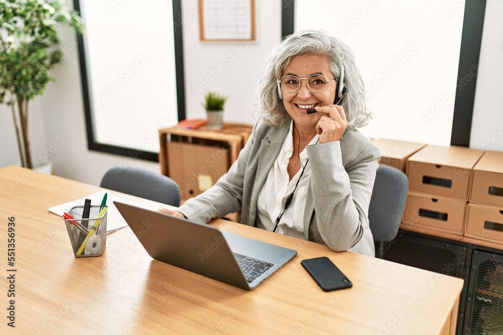 Middle age grey-haired call center agent woman smiling happy working at the office. Middle age grey-haired call center agent woman smiling happy working at the office.