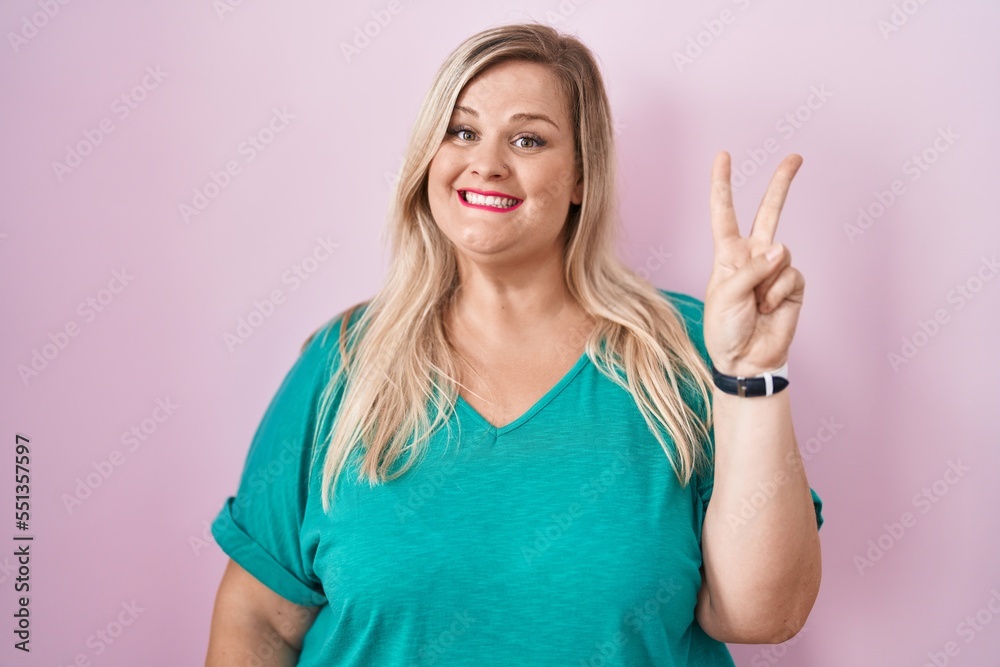 Caucasian plus size woman standing over pink background showing and pointing up with fingers number two while smiling confident and happy.