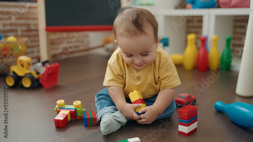 Adorable hispanic baby playing with construction blocks sitting on floor at kindergarten