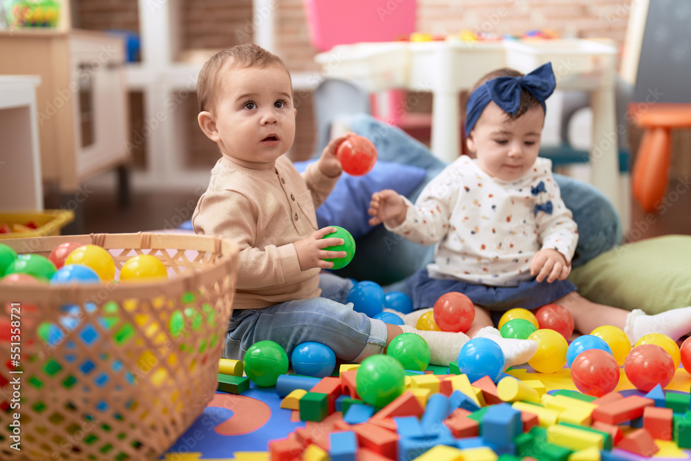 Two toddlers playing with balls sitting on floor at kindergarten Two toddlers playing with balls sitting on floor at kindergarten