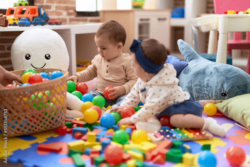Fototapeta premium Two toddlers playing with balls and xylophone sitting on floor at kindergarten