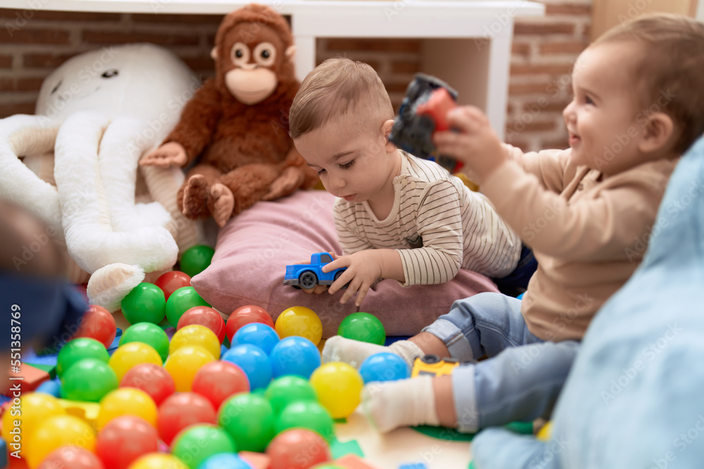 Two adorable toddlers playing with balls and car sitting on floor at kindergarten Two adorable toddlers playing with balls and car sitting on floor at kindergarten