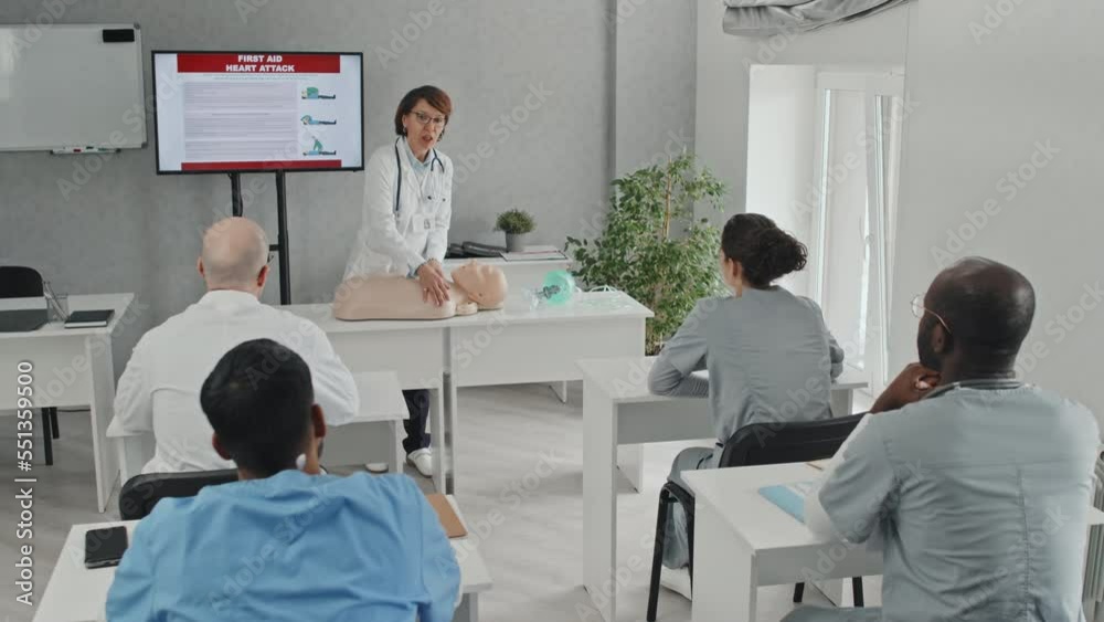 Mature doctor in white coat showing how to do heart massage to students at medical training course Mature doctor in white coat showing how to do heart massage to students at medical training course