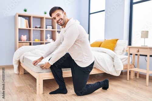 Young hispanic man smiling confident touching mattress at bedroom