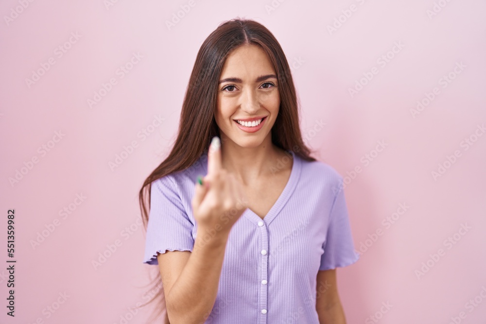 Young hispanic woman with long hair standing over pink background beckoning come here gesture with hand inviting welcoming happy and smiling Young hispanic woman with long hair standing over pink background beckoning come here gesture with hand inviting welcoming happy and smiling