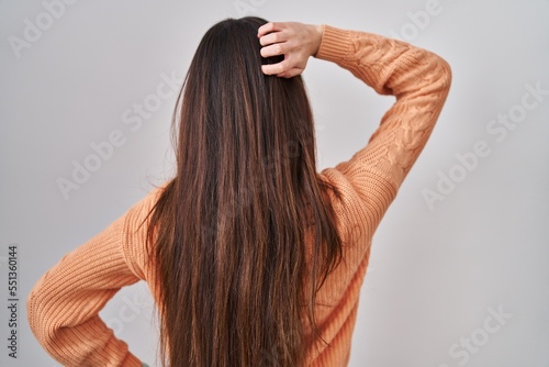 Young brunette woman standing over white background backwards thinking about doubt with hand on head