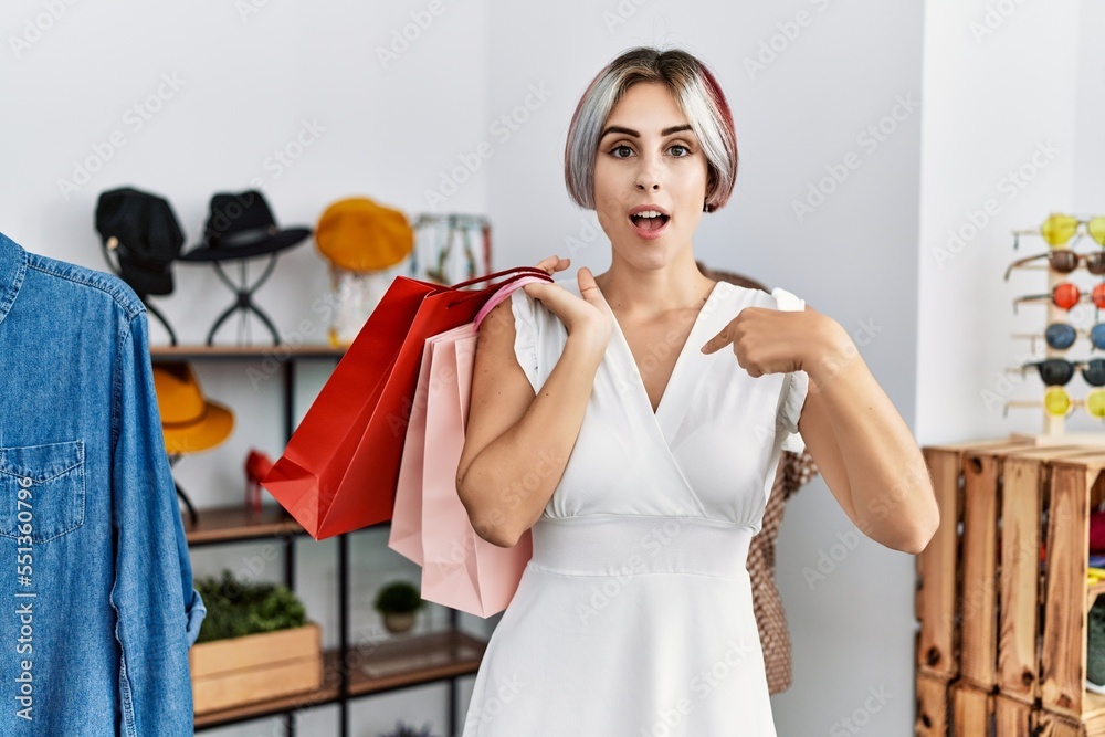 Young beautiful woman holding shopping bags at retail shop pointing finger to one self smiling happy and proud Young beautiful woman holding shopping bags at retail shop pointing finger to one self smiling happy and proud