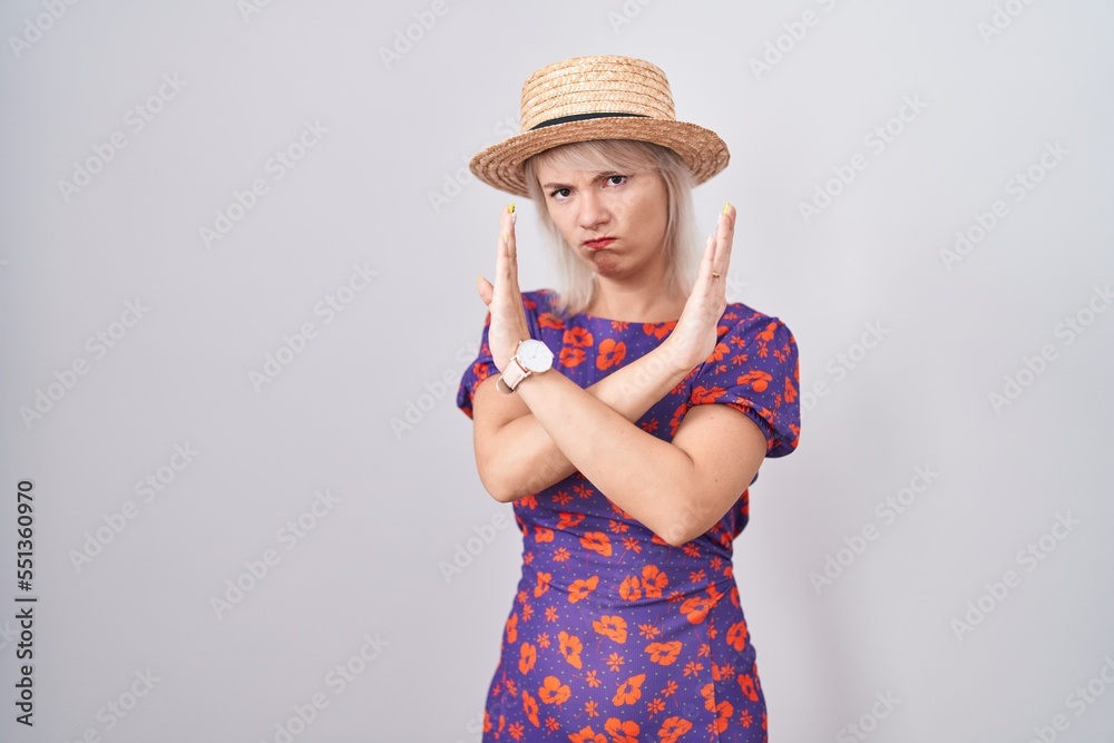 Young caucasian woman wearing flowers dress and summer hat rejection expression crossing arms doing negative sign, angry face Young caucasian woman wearing flowers dress and summer hat rejection expression crossing arms doing negative sign, angry face