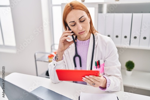 Young caucasian woman doctor using touchpad talking on smartphone at clinic