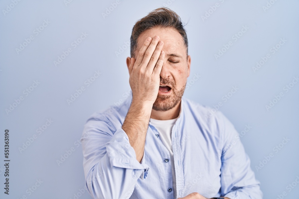 Middle age caucasian man standing over blue background yawning tired covering half face, eye and mouth with hand. face hurts in pain. Middle age caucasian man standing over blue background yawning tired covering half face, eye and mouth with hand. face hurts in pain.