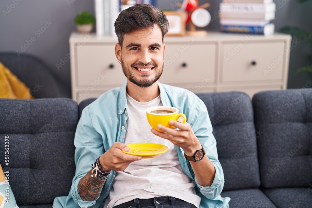Young hispanic man drinking coffee sitting on sofa at home Young hispanic man drinking coffee sitting on sofa at home