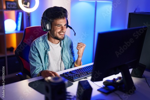 Young hispanic man streamer playing video game with winner expression at gaming room