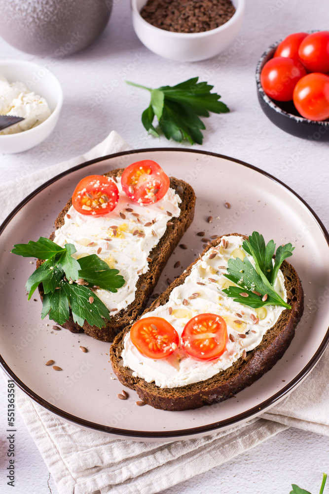 Sandwiches on rye bread with ricotta, tomatoes and parsley on a plate on the table. Vertical view Sandwiches on rye bread with ricotta, tomatoes and parsley on a plate on the table. Vertical view