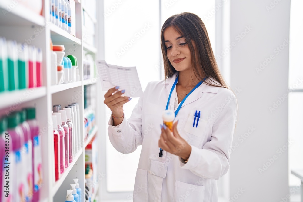 Young beautiful hispanic woman pharmacist holding pills bottle reading prescription at pharmacy