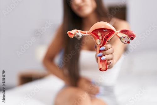 Young beautiful hispanic woman suffering for menstrual pain holding anatomical model of uterus at bedroom