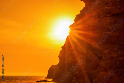 Woman tourist enjoying the sunset over the sea mountain landscape. Sits outdoors on a rock above the sea. She is wearing jeans and a blue hoodie. Healthy lifestyle, harmony and meditation