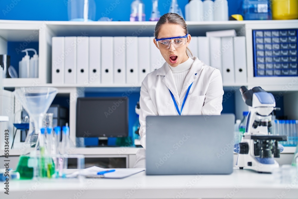 Young blonde woman working at scientist laboratory scared and amazed with open mouth for surprise, disbelief face