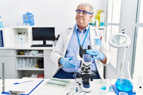 Senior caucasian man working at scientist laboratory smiling looking to the side and staring away thinking.