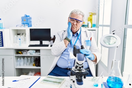 Senior caucasian man working at scientist laboratory touching mouth with hand with painful expression because of toothache or dental illness on teeth. dentist concept.