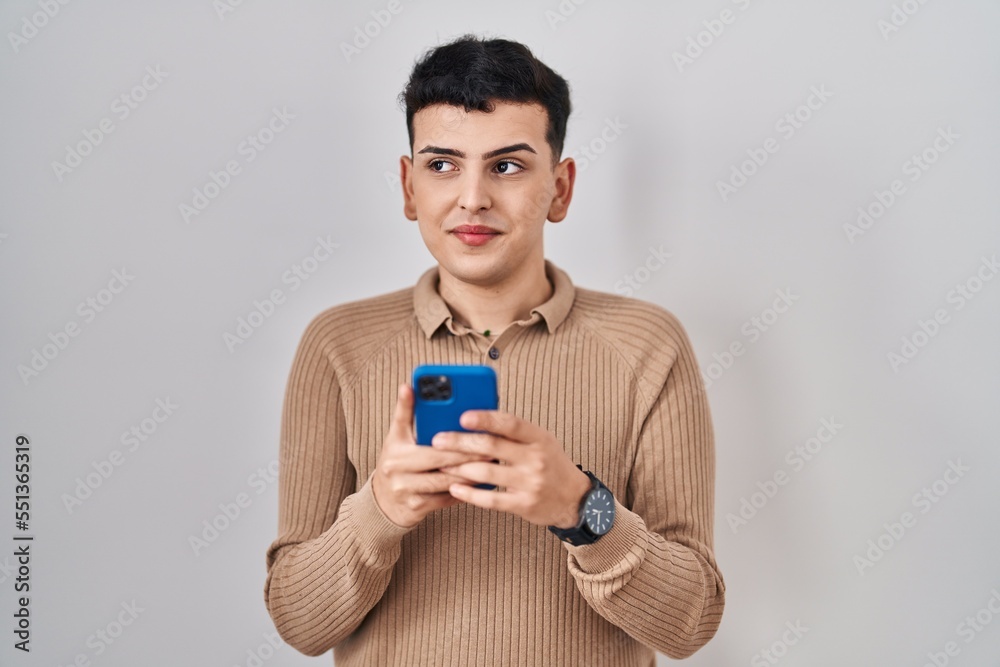 Non binary person using smartphone typing message smiling looking to the side and staring away thinking. Non binary person using smartphone typing message smiling looking to the side and staring away thinking.