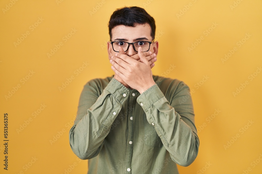 Non binary person standing over yellow background shocked covering mouth with hands for mistake. secret concept. Non binary person standing over yellow background shocked covering mouth with hands for mistake. secret concept.