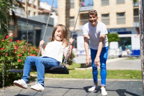Father and daughter smiling confident playing on swing at playground