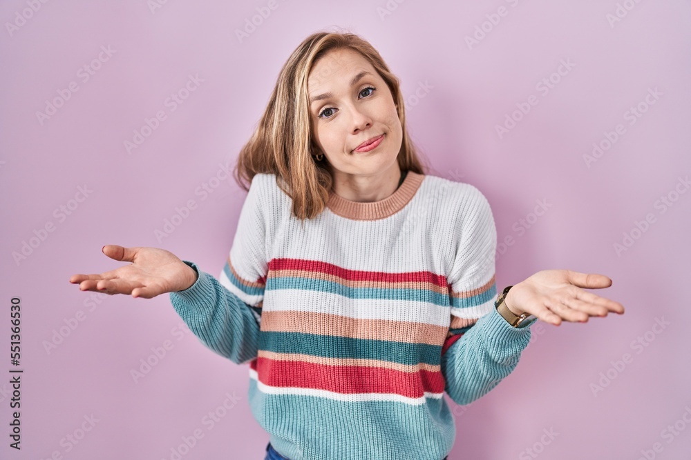 Young blonde woman standing over pink background clueless and confused with open arms, no idea concept. Young blonde woman standing over pink background clueless and confused with open arms, no idea concept.