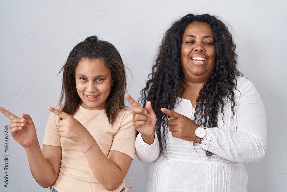 Mother and young daughter standing over white background smiling and looking at the camera pointing with two hands and fingers to the side.