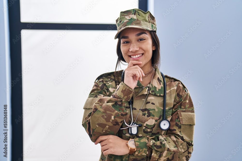 Young south asian woman wearing camouflage army uniform and stethoscope smiling looking confident at the camera with crossed arms and hand on chin. thinking positive.