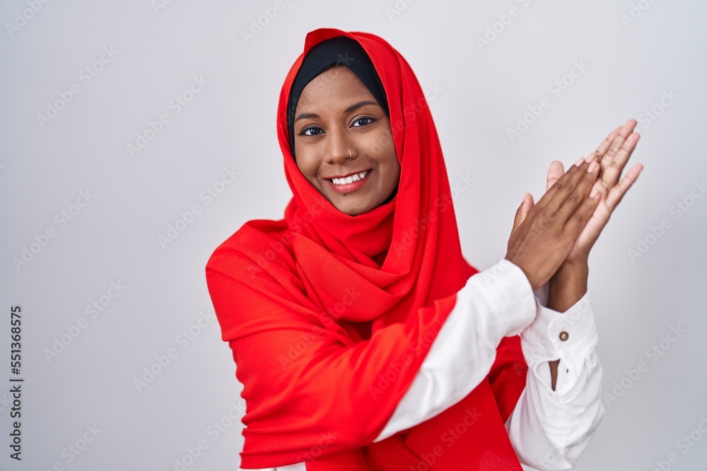 Young arab woman wearing traditional islamic hijab scarf clapping and applauding happy and joyful, smiling proud hands together Young arab woman wearing traditional islamic hijab scarf clapping and applauding happy and joyful, smiling proud hands together