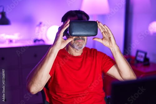 Middle age man streamer playing video game using virtual reality glasses at gaming room