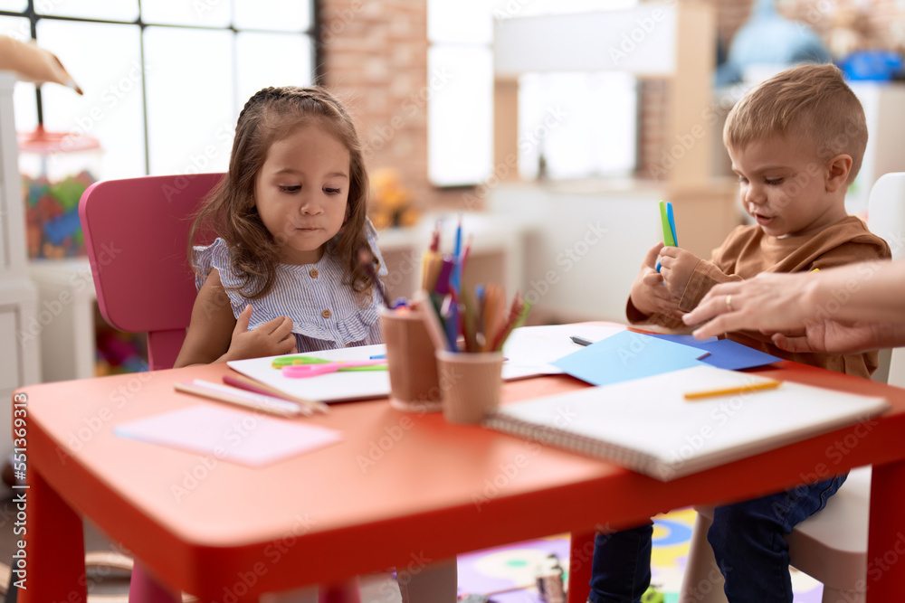 Adorable girl and boy sitting on table cutting paper at kindergarten Adorable girl and boy sitting on table cutting paper at kindergarten