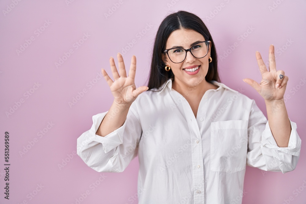 Young brunette woman standing over pink background showing and pointing up with fingers number eight while smiling confident and happy. Young brunette woman standing over pink background showing and pointing up with fingers number eight while smiling confident and happy.