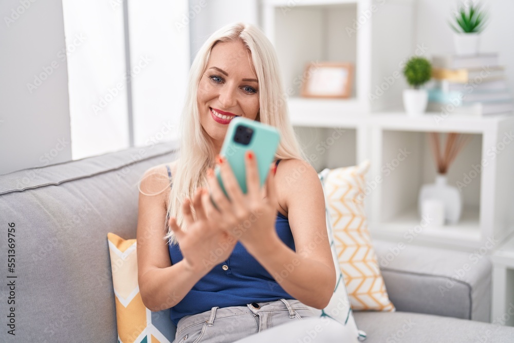 Young blonde woman using smartphone sitting on sofa at home Young blonde woman using smartphone sitting on sofa at home