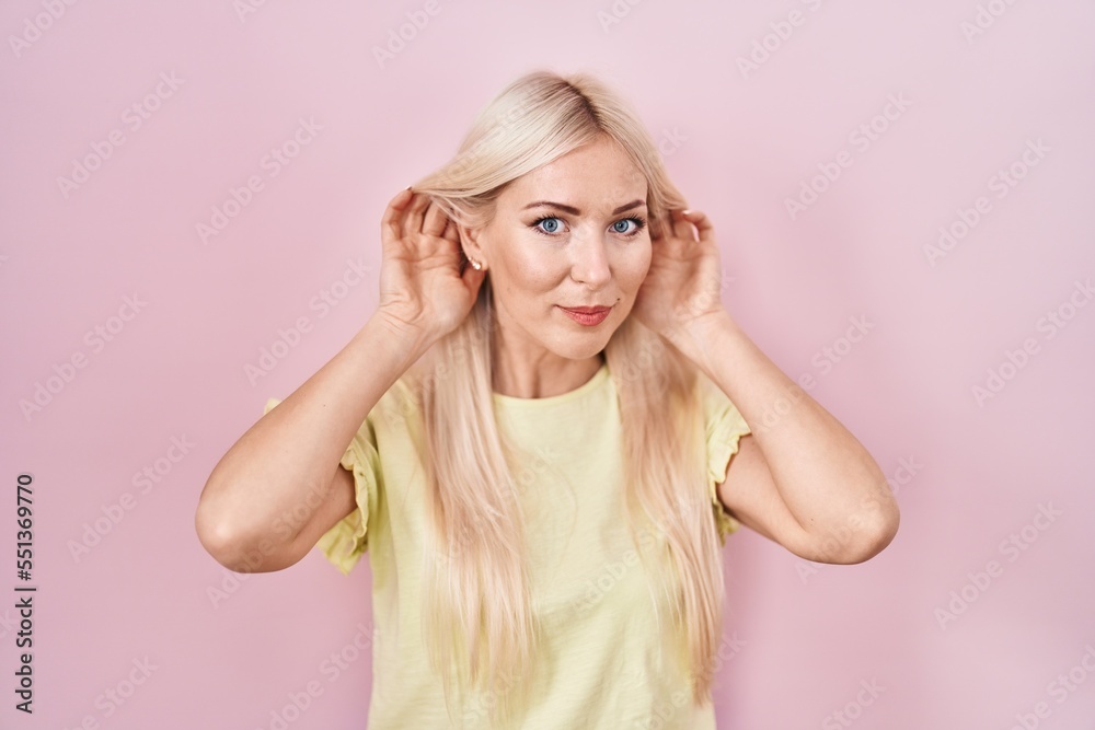 Caucasian woman standing over pink background trying to hear both hands on ear gesture, curious for gossip. hearing problem, deaf Caucasian woman standing over pink background trying to hear both hands on ear gesture, curious for gossip. hearing problem, deaf