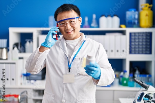 Young chinese man wearing scientist uniform using smartphone at laboratory