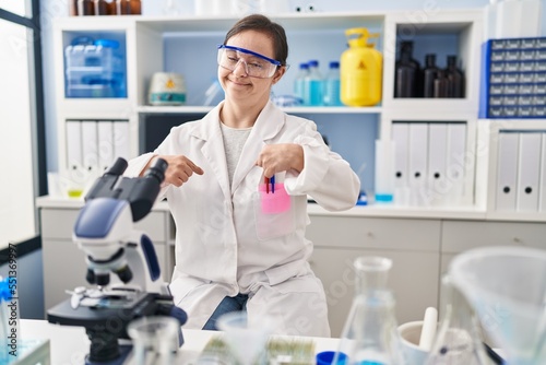 Hispanic girl with down syndrome working at scientist laboratory looking confident with smile on face, pointing oneself with fingers proud and happy.