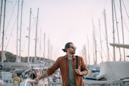 A young, stylish man in sunglasses at the marina among the sea yachts.